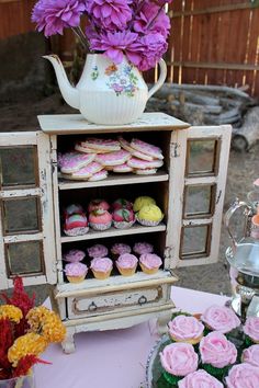 a table topped with lots of cupcakes next to a vase filled with flowers