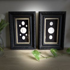 two framed pictures sitting on top of a wooden table next to a vase with flowers