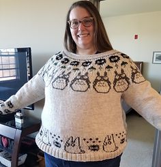 a woman standing in front of a computer monitor wearing a sweater with skulls on it