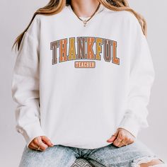 Show your appreciation for educators with this stylish "Thankful Teacher" sweatshirt! Made from premium Comfort Colors fabric, this cozy pullover is perfect for the fall season. The retro design and soft material make it a comfortable yet trendy addition to any teacher's wardrobe. Whether for Thanksgiving, a back-to-school gift, or a holiday surprise, this sweatshirt is a great way to show thanks. Perfect for everyday wear in and out of the classroom. Available in various sizes and colors, it's an essential piece for any teacher's collection. This custom crewneck sweatshirt brings both incredible quality and amazing style to the mix. Made with soft, ring-spun cotton fabric with 100% cotton threads, it sits unmatched when it comes to softness. All sweatshirts feature a rolled forward should Winter School Sweatshirt With Letter Print, Winter Letter Print Sweatshirt For School, Fall School Hoodie With Letter Print, College Long Sleeve Sweatshirt For Fall, Long Sleeve Sweatshirt For College In Fall, School Spirit Cotton Hoodie For Fall, Fall Long Sleeve College Sweatshirt, White Tops For School In Fall, Fall School Fleece Sweatshirt