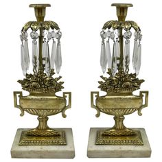 a pair of antique brass candlesticks with crystal beads and leafy decorations on marble bases