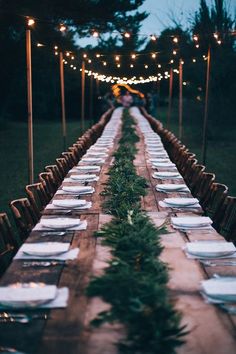 a long wooden table with white plates and place settings set up for an outdoor dinner