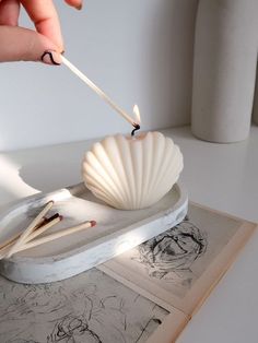 a person holding a toothpick over a shell on top of a drawing board