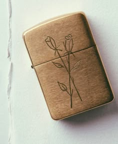 a flask shaped like a lighter with flowers etched on the front and sides, sitting on a white surface