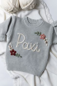 a knitted sweater with the word poss on it next to two balls of yarn