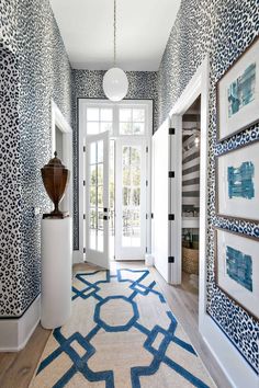 the hallway is decorated with blue and white wallpaper, an area rug, and two vases on either side of the door