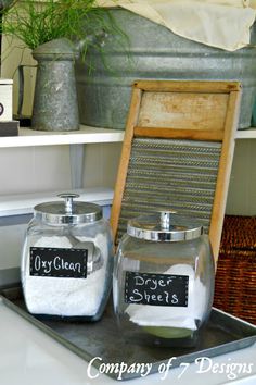 two glass jars with labels on them sitting on a tray in front of a potted plant