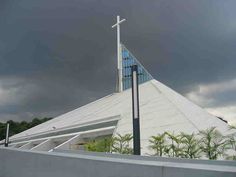 a large white building with a cross on it's roof and trees in the background