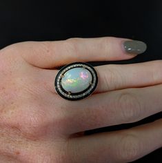 This statement ring features a 7.49 carat oval opal gemstone of size 16x12 mm with a halo of natural earth mined diamonds and black enamel detail, all set in solid 14K gold. This ring can be a beautiful October birthstone gift for your loved ones! This ring is made with solid 14K Gold and natural Earth mined SI / G-H diamonds. As listed, this ring is ready to ship. If you're interested in purchasing this setting with a different center stone please message us! Oval Opal Ring With Polished Finish In Fine Jewelry, Oval Opal Ring With Polished Finish, Heirloom Oval Cabochon Opal Ring, Heirloom Oval Opal Ring Collectible, Fine Jewelry Oval Opal Ring With Polished Finish, Classic Oval Opal Jewelry, Oval Opal Gemstone Jewelry, Black Oval Opal Ring For Formal Occasions, Fine Jewelry Oval Cabochon Opal Ring