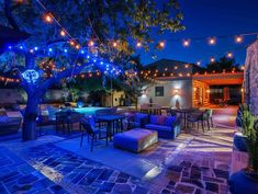 an outdoor dining area with lights strung from the trees and patio furniture set up in front of it