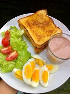 a white plate topped with an egg, toast and salad next to a cup of juice