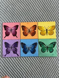 four different colored butterflies are shown on a table with a person's hand in the foreground