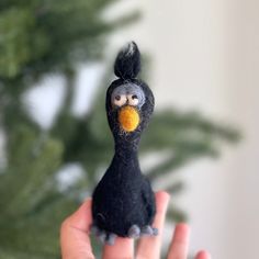 a hand holding a small black bird with an orange ball in it's beak