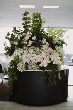 an arrangement of flowers in a black planter on the floor at a wedding reception