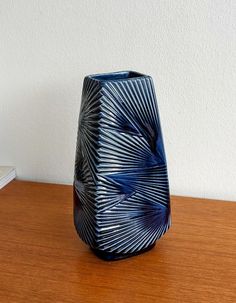 a blue vase sitting on top of a wooden table next to a white wall and a book