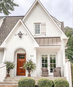 a white brick house with two chairs and potted plants on the front steps in front of it