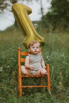 a baby sitting in a chair with a number one balloon on it's back