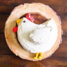 a cake decorated like a chicken sitting on top of a wooden bowl filled with frosting