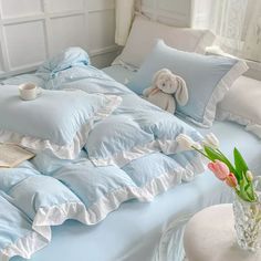 a bed with blue sheets and white ruffles has a stuffed animal on it