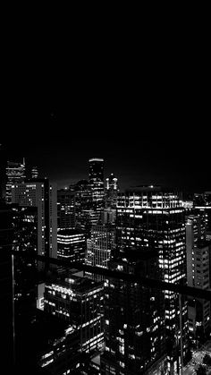 black and white photo of city at night with lights in the windows, skyscrapers lit up