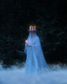 a woman dressed as a ghost with candles in her hand, standing in the snow