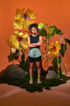 a woman standing in front of flowers with her arms crossed