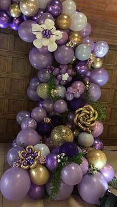 a purple and gold balloon arch with flowers on the top, surrounded by other balloons