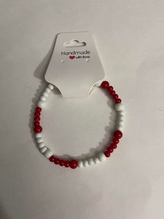 A bracelet with red and white beads fastened on a clear elastic cord (one size fits most) Cheap Red Beaded Bracelets With Letter Beads, Cheap Red Beaded Bracelets, Red And White Beaded Bracelet, Trendy White Beaded Bracelets, Trendy Red Beads For Gifts, Adjustable Red Letter Beads, Handmade White Casual Beads, Casual White Hand-strung Wristband, Red Wristband Bracelet With Colorful Beads