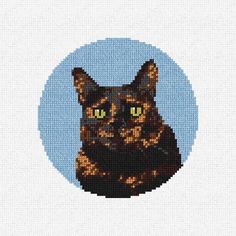 a cross - stitch picture of a cat with green eyes in a blue circle on a white background