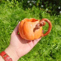 a hand holding an orange ceramic pumpkin shaped cup