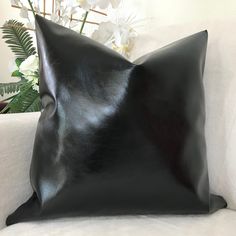 a black pillow sitting on top of a white couch next to a vase with flowers