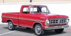 an old red pickup truck parked in a parking lot next to a white wall and building