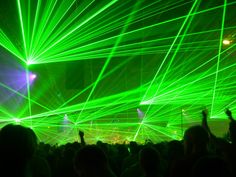 green laser lights are shining in the night sky over a crowd at a concert with their hands up