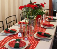 the table is set with red and white plates, napkins, silverware, and flowers