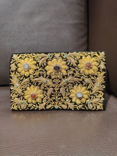 Beautiful hand-embroidered floral silk clutch bag inlaid with semi-precious stones. The front is completely covered in the design and has a closure flap with magnettic snap fastening. This clutch is perfect for daytime or night time. It is the ideal size for fitting all your essentials. It is a stylish accessory for each & every occasion. This equisite piece is even ideal for gifting to your near & dear one's . Thread - Silk Fabric - Velvet Variety of Semi-precious stones are used in this piece Zardozi is a type of heavy and elaborate metal embroidery on silk, satin, or velvet fabric base. Designs are often created using gold and silver wires and can incorporate pearls, beads, and precious stones. The embroidered silk clutch bag is made in Agra, India & is fully handmade. Designed to compl Festive Rectangular Clutch With Gold Embroidery, Rectangular Clutch With Gold Embroidery For Festivals, Rectangular Gold Embroidery Clutch For Festivals, Rectangular Gold Embroidered Clutch For Festivals, Gold Evening Bag With Intricate Embroidery For Receptions, Gold Embroidered Clutch For Festivals, Designer Embroidered Rectangular Clutch, Luxury Clutch With Gold Embroidery For Reception, Traditional Embellished Clutch For Festivals