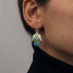 Introducing our Handcrafted Love Angel Earrings, the perfect embodiment of divine elegance, ideal for gifting that special someone or treating yourself to a touch of heavenly charm. These earrings are meticulously crafted with sterling silver and adorned with the vibrant allure of Cloisonné Enamel. The unique technique used in their creation breathes life into the design, making each pair truly unique. A testament to high-quality craftsmanship, the earrings are made from 925 sterling silver, ensuring durability and long-lasting shine. Key Features: - Handmade Love Angel Earrings - Compact size, measuring just 0.8 inches (2cm) long - Crafted from premium 925 Sterling Silver - Adorned with radiant Cloisonné Enamel - Arrives in a beautiful, branded gift box These earrings don't just make a st Artistic Dangle Jewelry As Gift, Artistic Dangle Jewelry For Gifts, White Sterling Silver Pendant Earrings, Artistic Design Dangle Jewelry Gift, Artisan Earrings With Artistic Design As A Gift, Artisan Earrings With Artistic Design For Gift, Artisan Jewelry With Ear Wire For Gifts, Artisan Pierced Jewelry As Gift, Artistic Enamel Jewelry With Matching Earrings