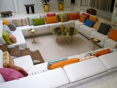 a living room filled with lots of white couches and colorful pillows on top of each other