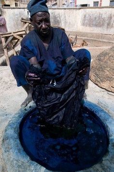 a man sitting on top of a rock next to a blue water hole in the middle of town