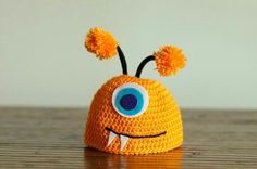 an orange crocheted hat with googly eyes and two pom poms