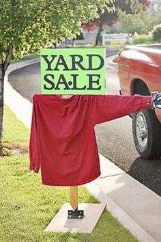 a yard sale sign on a wooden stand in front of a red car with a green yard sale sign attached to it