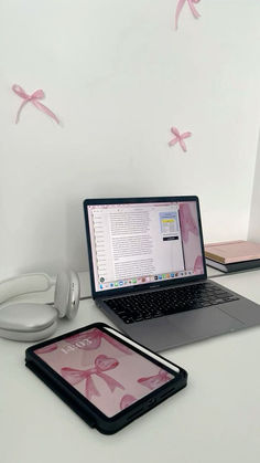 an open laptop computer sitting on top of a white desk next to a pink tablet