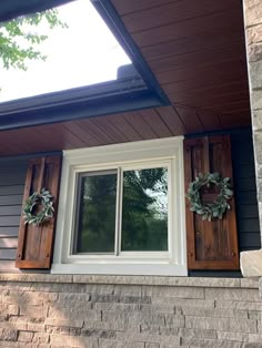 two wreaths are hanging on the window sill in front of a brick house