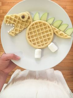 a white plate topped with waffles and fruit shaped like a crocodile face on top of it