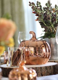 a copper pumpkin sitting on top of a wooden table next to glasses and vases