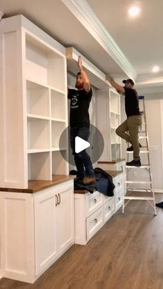 two men are standing on top of white cabinets and one man is climbing up the ladder