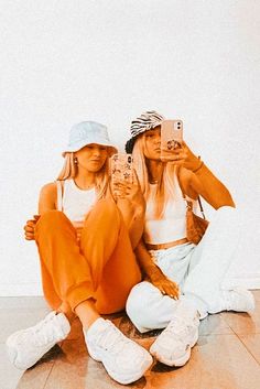 two young women sitting on the floor taking pictures with their cell phones and looking at them