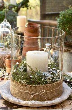 an image of a candle in a glass container with greenery on the bottom and candles inside