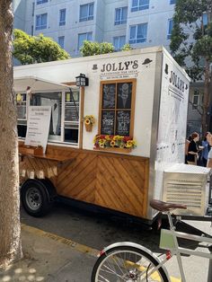 a food truck parked next to a tree on the side of the road in front of a building