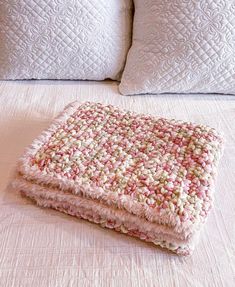 a pink and white blanket sitting on top of a bed next to two pillow cases