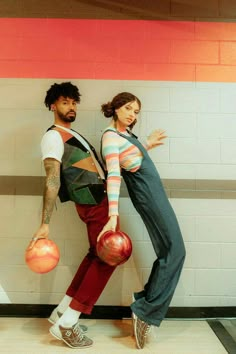 a man and woman standing next to each other holding bowling balls in front of a wall